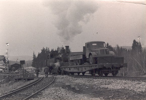   Historická fotografie z poloviny padesátých let 20. století ze stavby přeložky trati Černá v Pošumaví - Nová Pec (Želnava). Na obrázku vlevo odbočuje již odpojená kolej původní trati, vpravo manipuluje pára 423.060 s plošinovým vagónem, loženým sklápěcí Tatrou 111. Takto byl u stanice Nová Pec dosypáván násep pro zapomenutý pěšunk.  